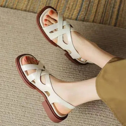 Women's glossy patent leather sandals with cross-belt straps, square toe, and a low block heel.
