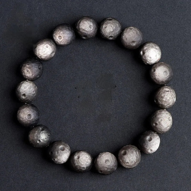 Natural obsidian crater ball bracelet showing polished spherical beads in silver stone meteorite colour with visible mineral texture