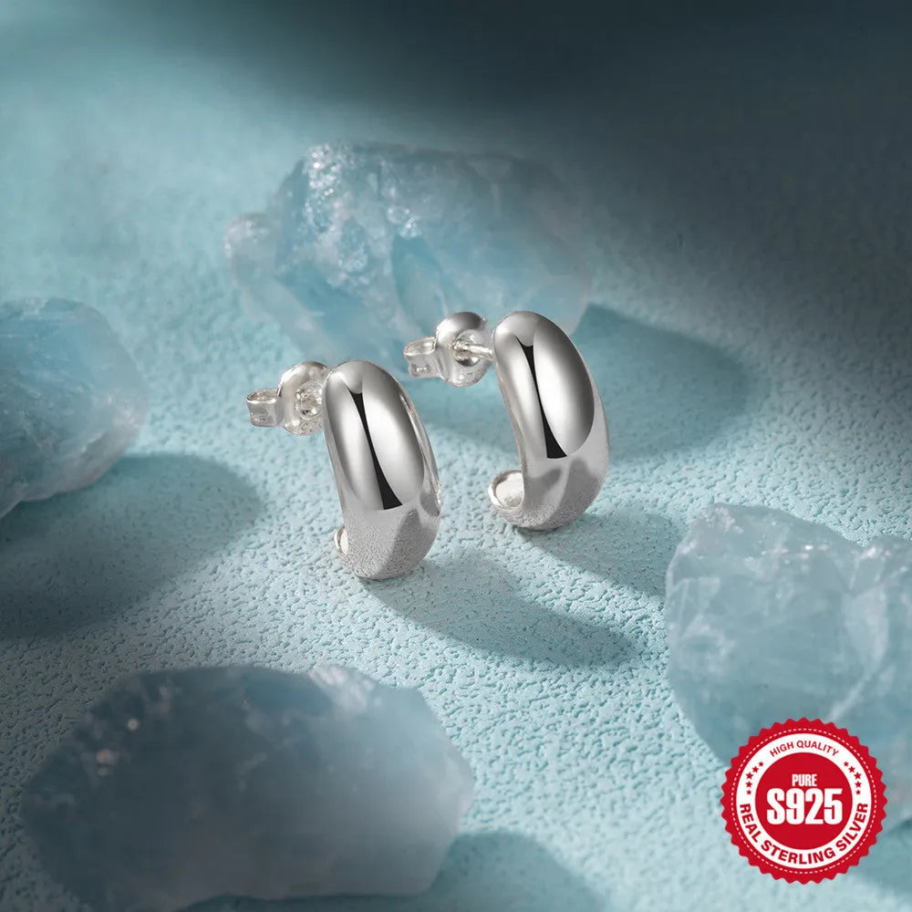 Close-up of a glossy C-shaped sterling silver stud earring with a gold electroplated finish.