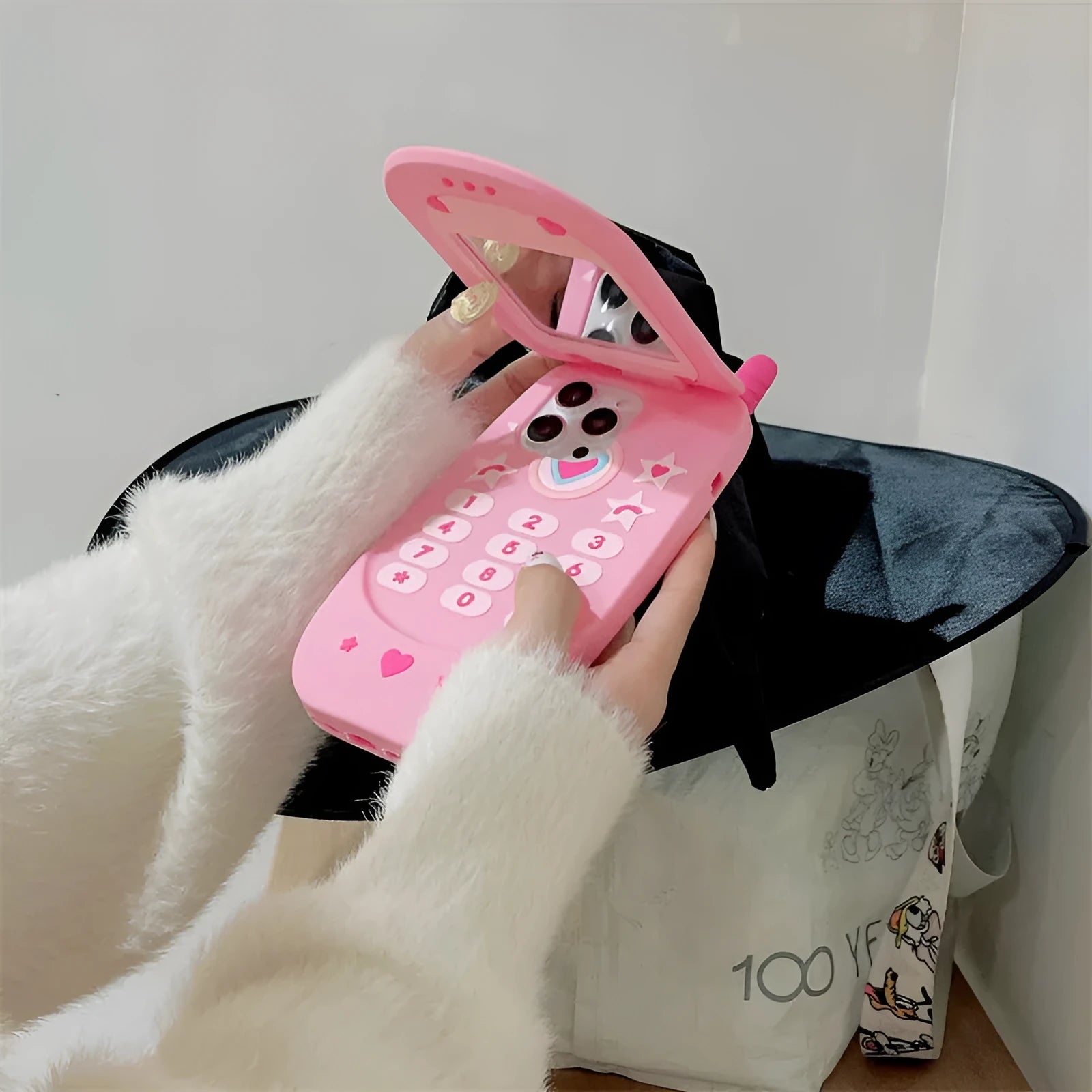 Light pink silicone flip phone shape case with mirror for iPhone, showing cute cartoon style.