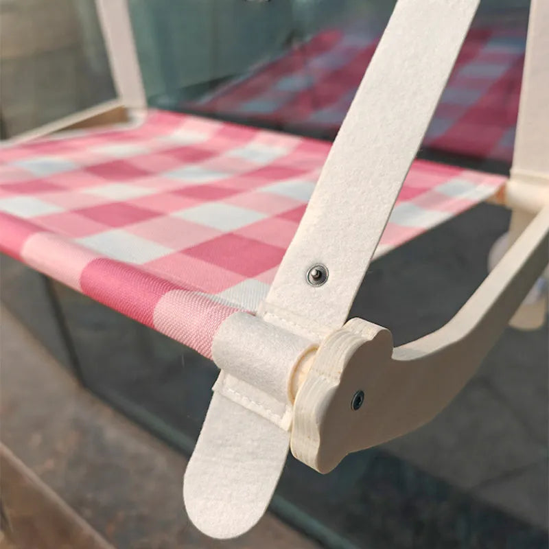 Pink wooden cat hammock bed with suction cups attached to a window, showing a cat lying on the linen mat.