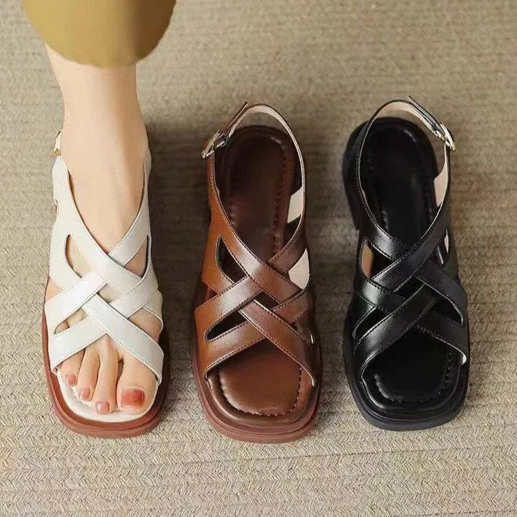 Women's glossy patent leather sandals with cross-belt straps, square toe, and a low block heel.