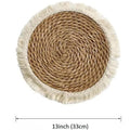 Round natural papyrus straw placemat with decorative tassel edge on a wooden table.
