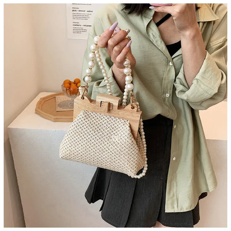 Women's woven straw shoulder bag with pearl chain strap in beige, showing its horizontal square shape.