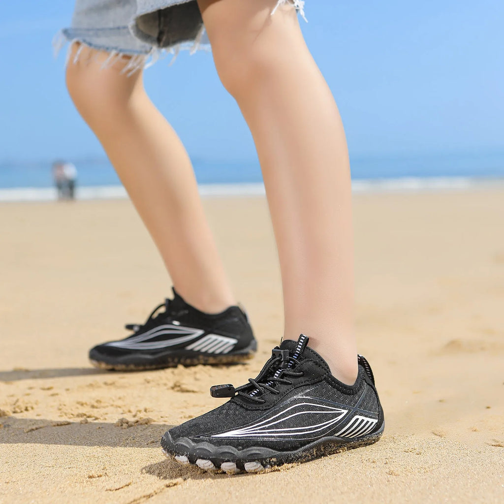 Children's elastic band wading shoes in grey with non-slip rubber sole, shown on a beach.