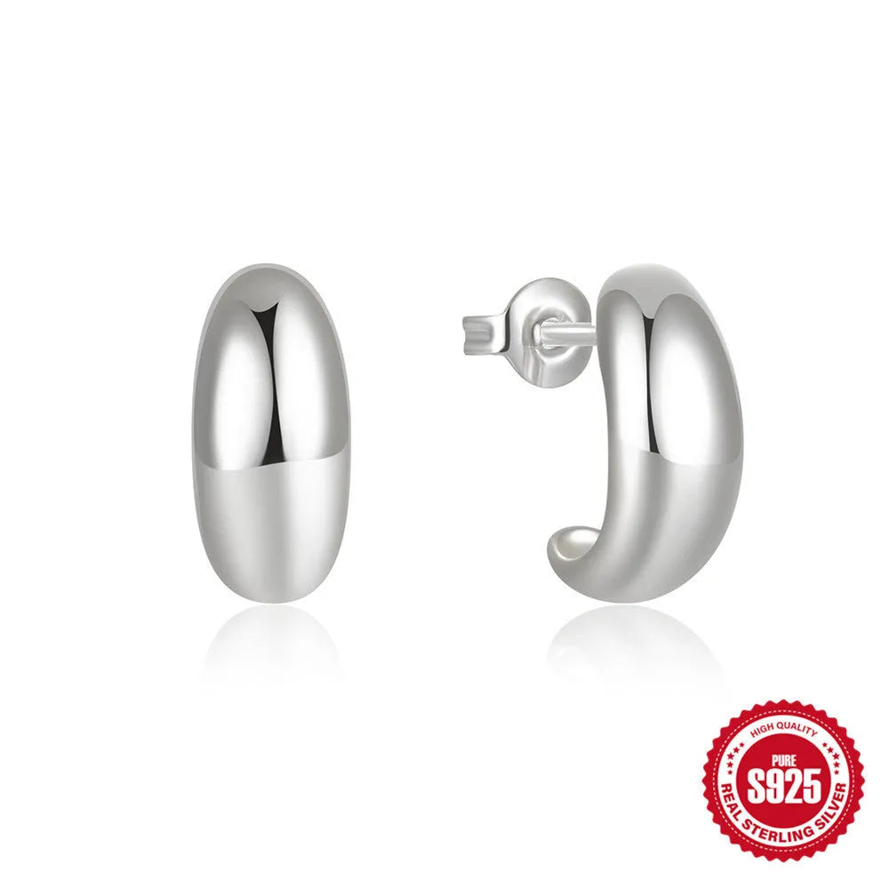 Close-up of a glossy C-shaped sterling silver stud earring with a gold electroplated finish.